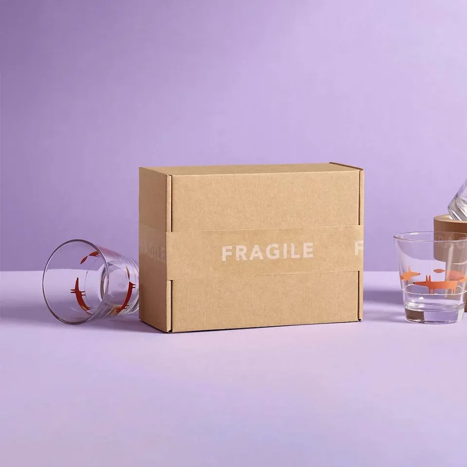 Fragile Goods Mailer Boxes: Plain kraft mailer wrapped in a printed paper band with a handling warning, beside glasses